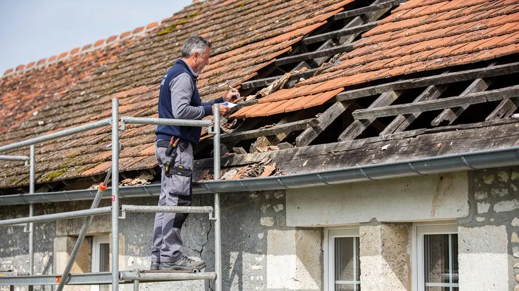 Building surveyor inspecting terracotta roof tiles and structure on scaffolding at a French historic property