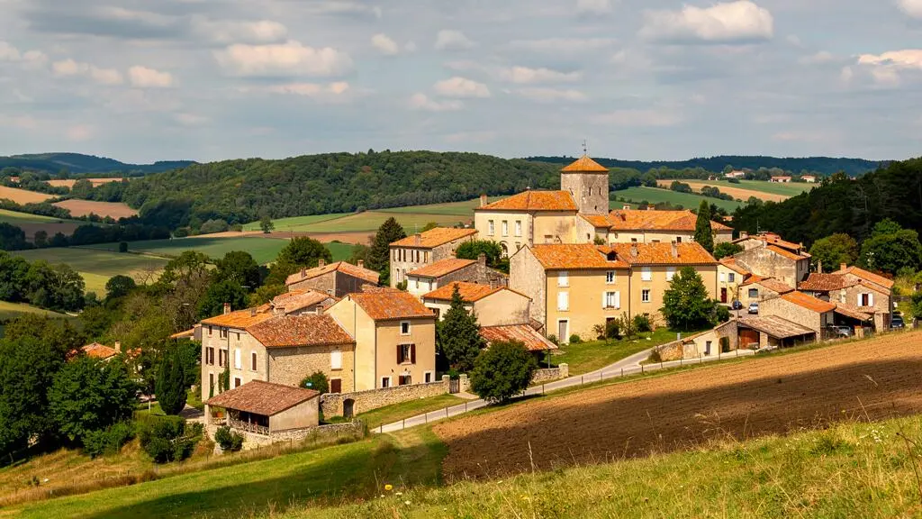 Traditional honey-stone village with terracotta roofs on a hillside surrounded by rolling countryside in South-West France